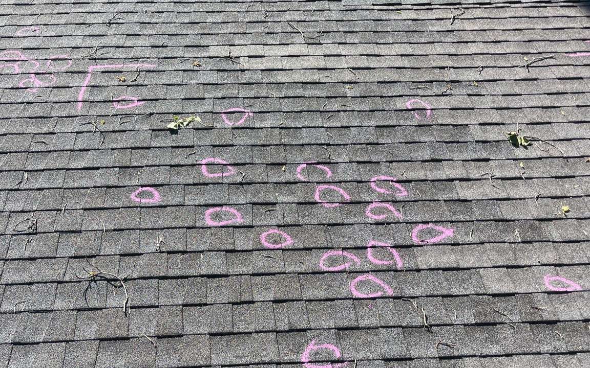 Hail hits on asphalt shingles circled in chalk during a roof inspection