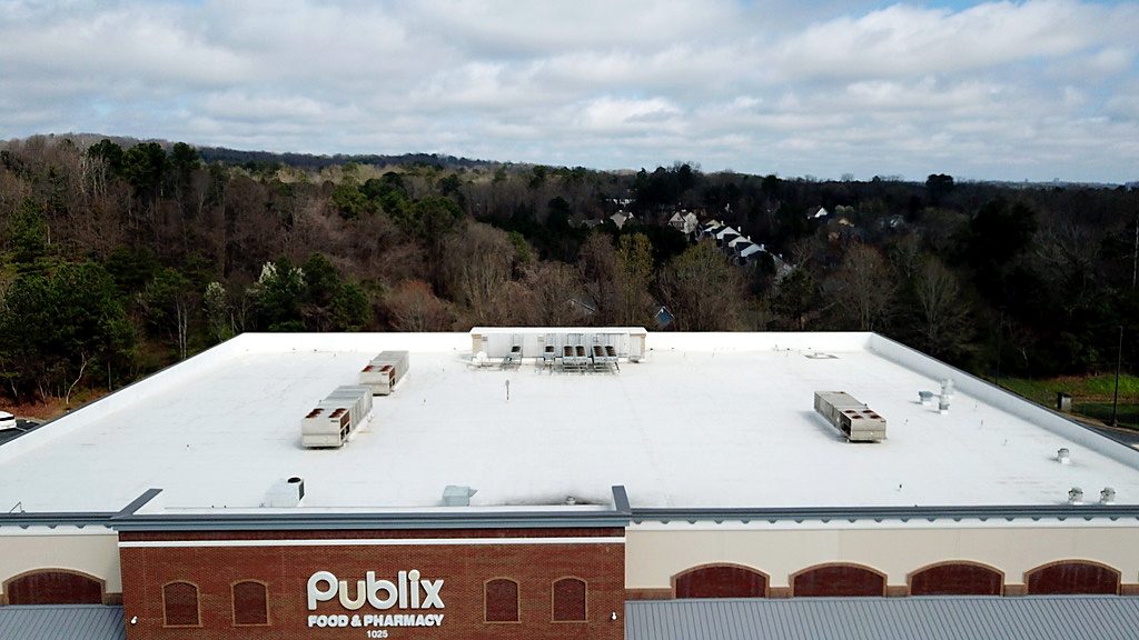 A white single-ply membrane roof on a grocery-anchored retail building, every rooftop unit and curb flashed in