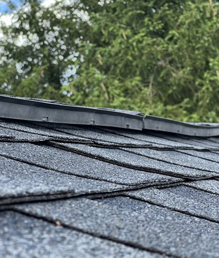 A ridge vent on an asphalt shingle roof lifting away from the shingles, leaving a visible gap.