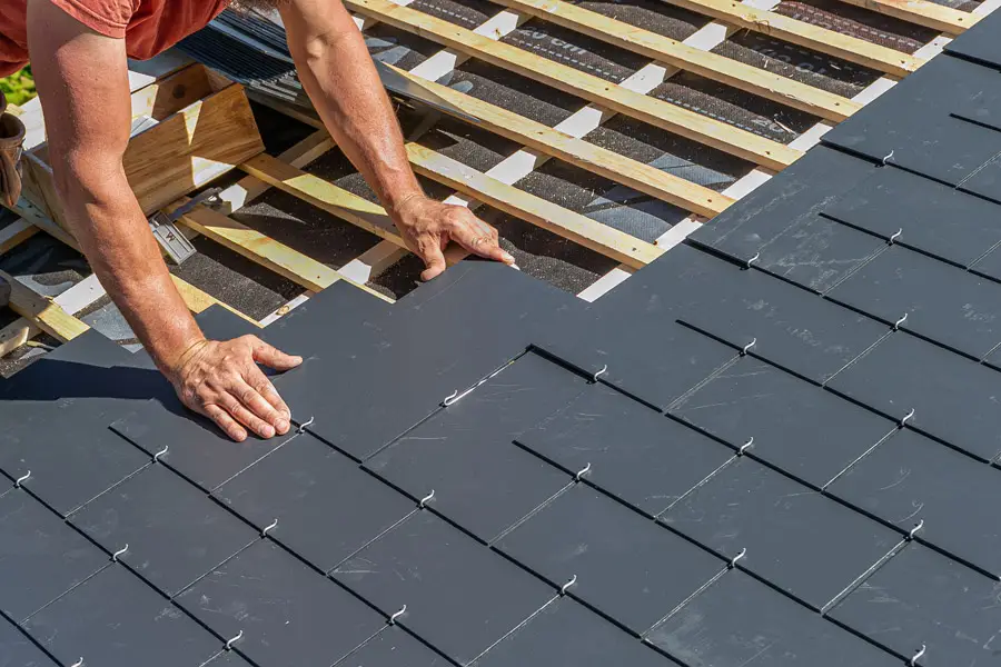 Experienced worker installing slate roofing tiles, showcasing precision and craftsmanship, with wooden framework visible beneath the slate.